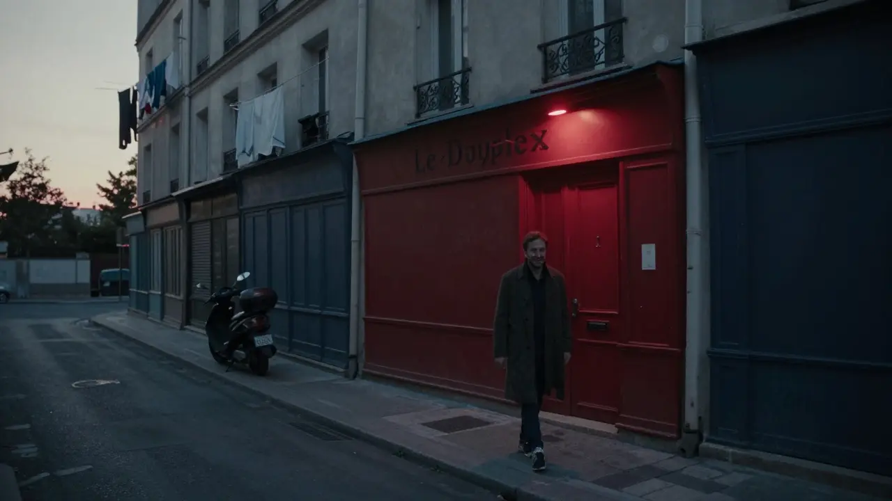 A lone person leaving Le Duplex at dawn, the red light still glowing behind them on a quiet Paris street.