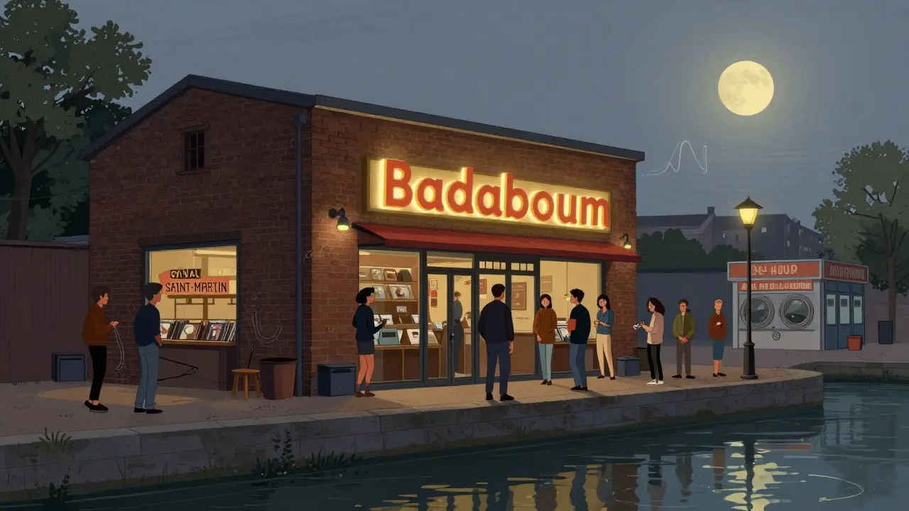 Exterior of Badaboum club at night with glowing sign, line of people waiting, canal and vintage shops in background.